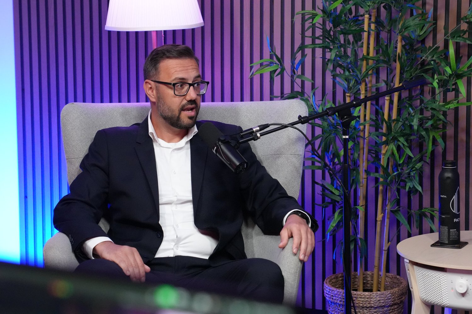 Man with glasses in a plush armchair speaking into a microphone