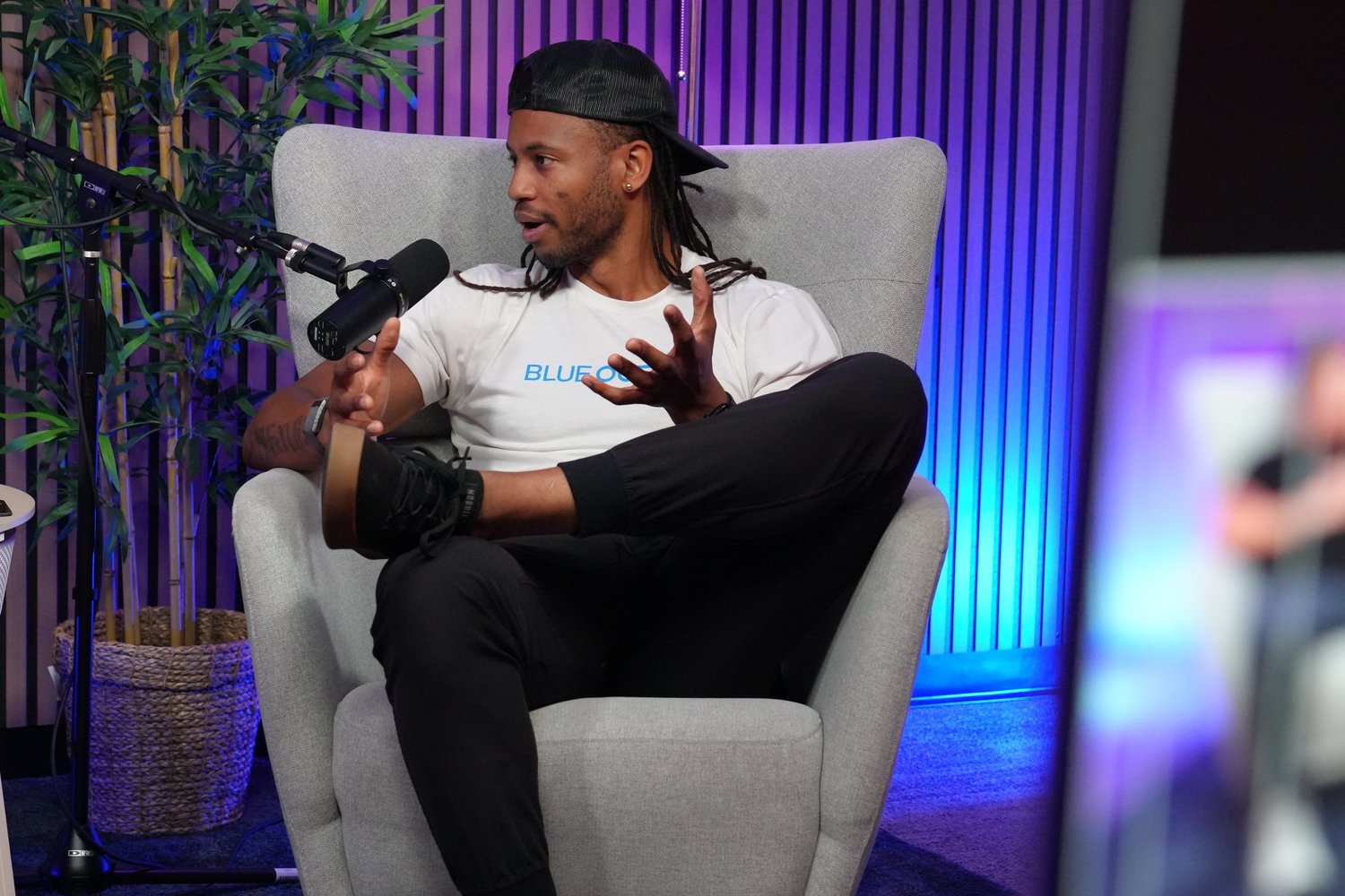 Man with locs in an armchair speaking into a microphone