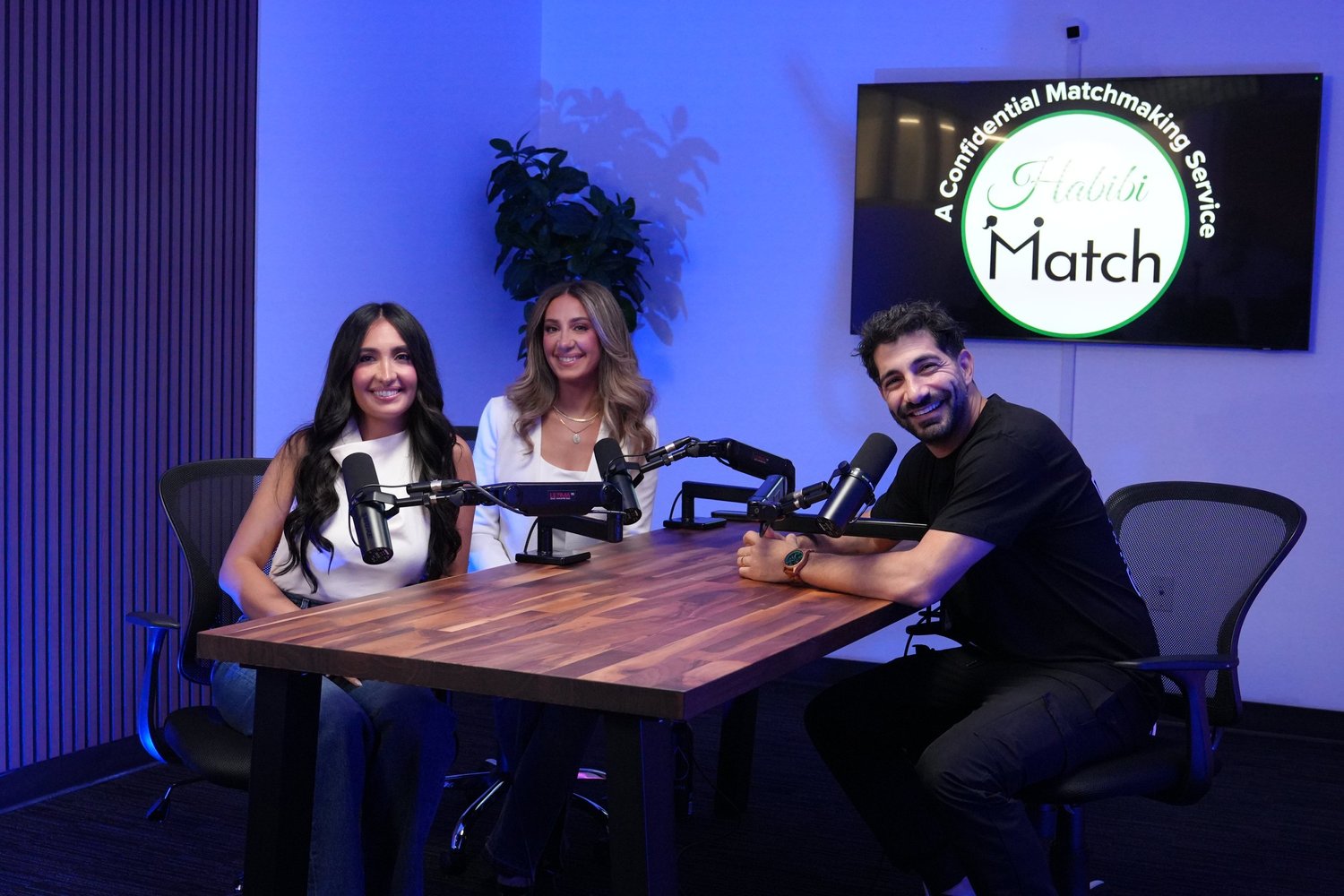Three people at a table with a large screen behind them
