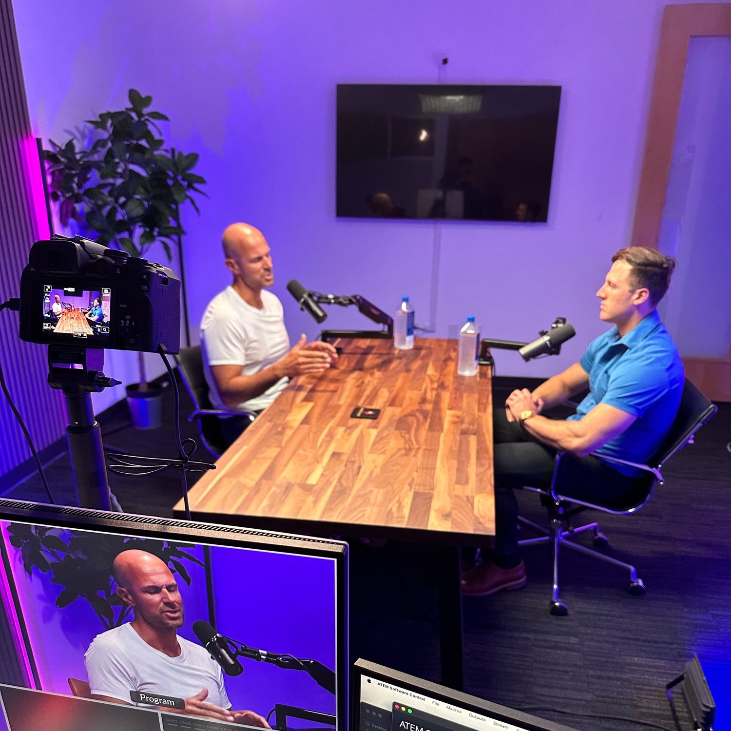 Two men at a wooden table recording a podcast with a camera