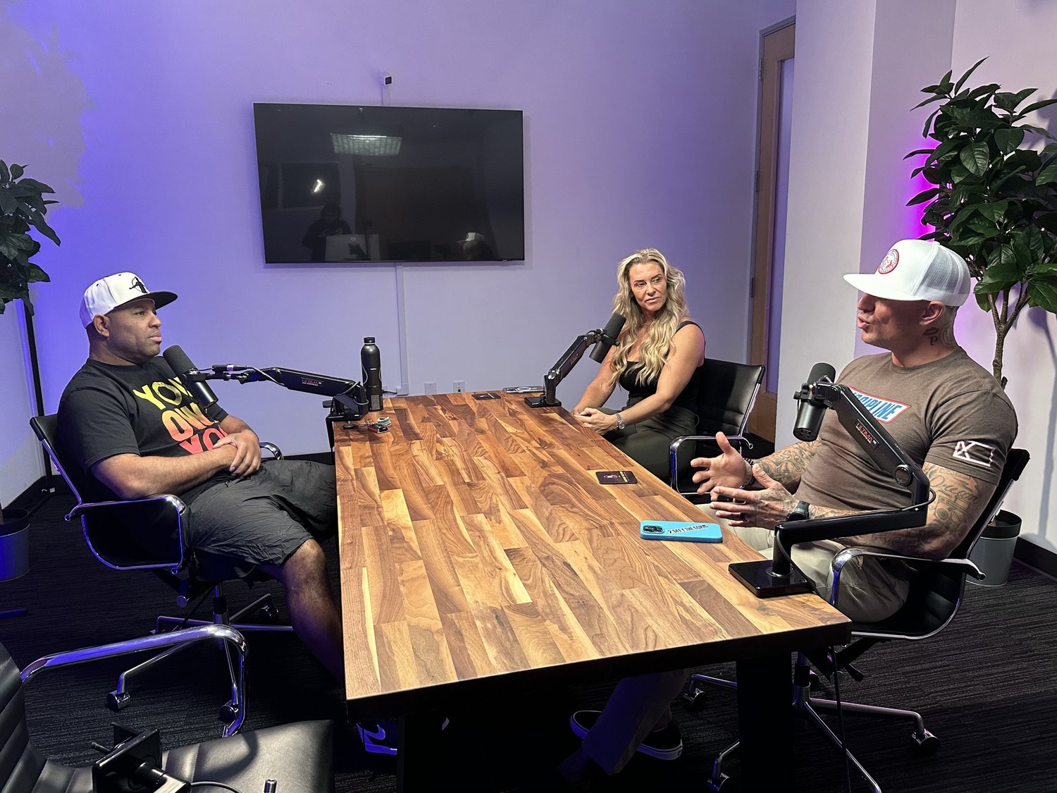 Three people recording a podcast around a wooden conference table with microphones